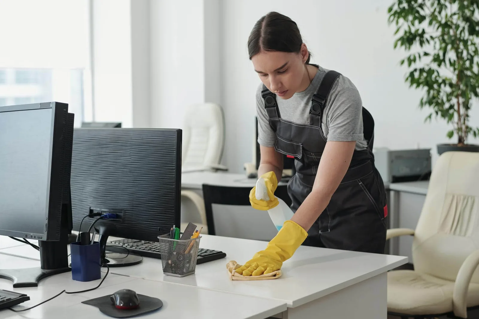Cleaner disinfecting a desk in a bright office